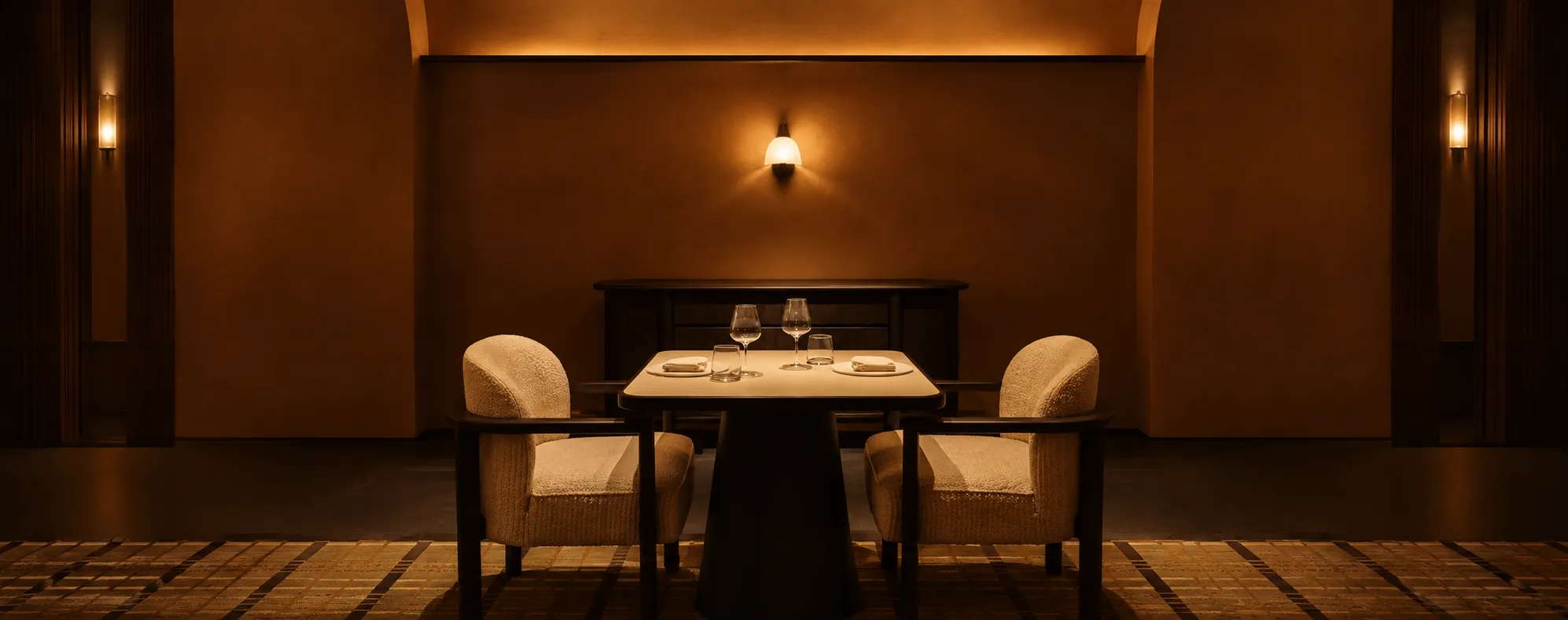 Warm, intimate fine-dining restaurant interior with a table set for two under soft amber lighting.